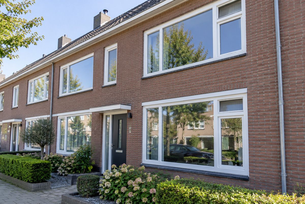 Nederlandse rijtjeswoningen met witte kunststof kozijnen, grote ramen en draaikiepramen in de voorgevel